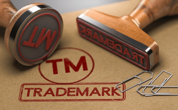 An image showing a wooden stamp creating a "TRADEMARK" seal on paper, alongside text debunking four common myths about trademark ownership and registration.