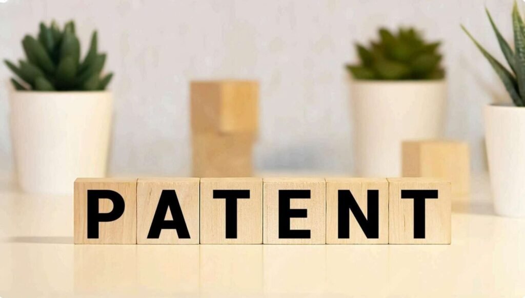 Wooden blocks spelling PATENT on a professional desk, illustrating the three types of patent protection in India: Utility, Design, and Process.