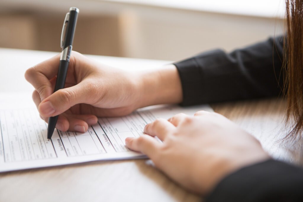 A person signing a document, representing a startup applicant filing Form 18A for fast-track patenting in India.
