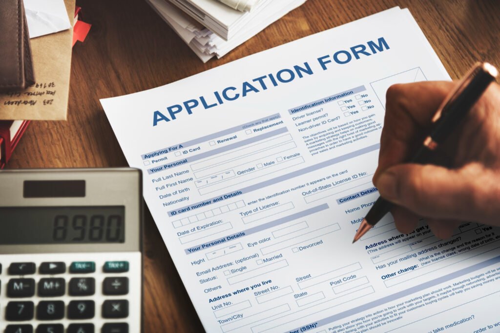 Hand filling out an application form next to a calculator.
