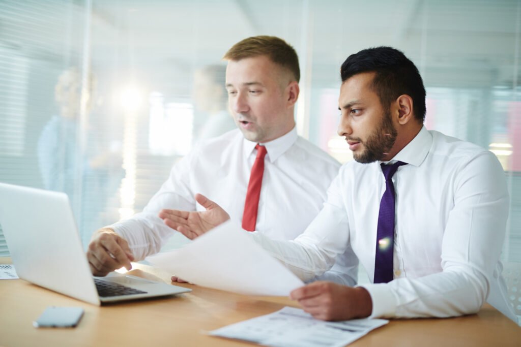 Two business professionals collaborating over a laptop and documents to discuss patent licensing strategies.