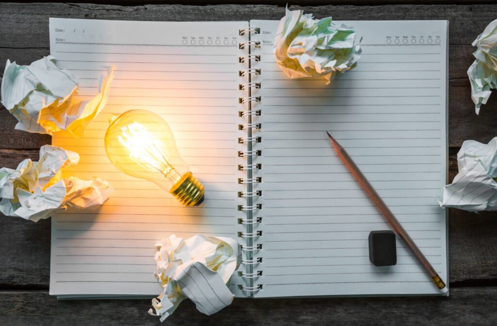 Open notebook with a glowing lightbulb and crumpled paper representing a patent application.