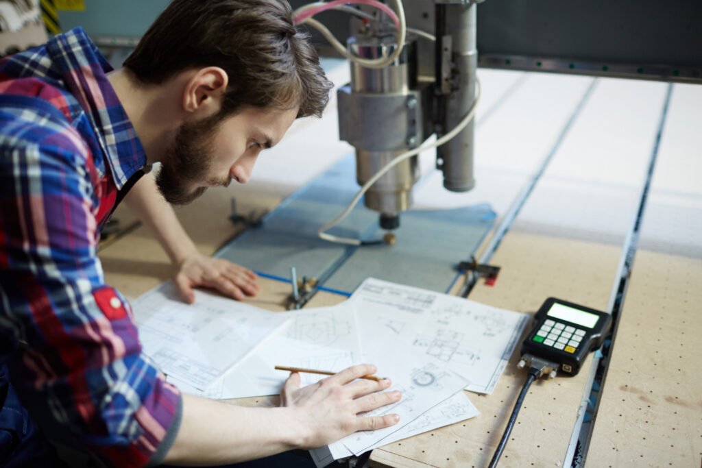 Designer examining blueprints and technical drawings next to manufacturing equipment.